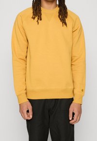 Felpa gialla a girocollo con polsini e orlo a coste, caratterizzata da un logo sull manica. Tessuto morbido con una vestibilità comoda.