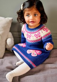 Rochie tricotată de culoare albastră, cu accente roz în formă de fluturi, guler rotund și un yoke cu model. Prezintă colanți albi și un fundal texturat de culoare gri.