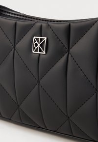 Juodas siuvinėtas rankinukas, pagamintas iš lygaus odos, su siuvinėta deimanto rašto struktūra ir sidabriniu logotipu priekyje.