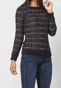 Zwarte trui met kleurrijke horizontale strepen, textuur stof, ronde hals en aansluitende mouwen. Gekocht met donkerblauwe spijkerbroek.