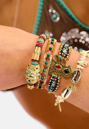 Collection de six bracelets composés de perles turquoise, rouges et dorées, avec un fermoir en or et des accents en coquillage. Diverses textures et motifs.