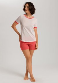 Conjunto de cama de algodón que incluye una parte superior blanca de manga corta con ribete rojo y pantalones cortos rosas. La tela parece suave con texturas lisas.