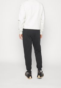 Ljusgrå crewneck sweatshirt med ribbade ärmar, matchad med svarta smalrandiga sweatpants med bakficka och elastiska muddar, bärs med svarta sneakers.