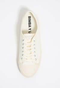 Beige canvas sneaker with round toe, white rubber outsole, and silver eyelets. Laces run through six pairs of eyelets, featuring brand logo inside.