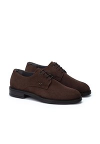 Zapatos derby de ante marrón con punteras redondas y cordones negros. Presentan un sutil detalle de costura y una suela de goma negra lisa.