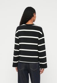 Haut à manches longues rayé noir et blanc avec un col rond et une coupe décontractée, doté de larges manches et d'un tissu texturé.