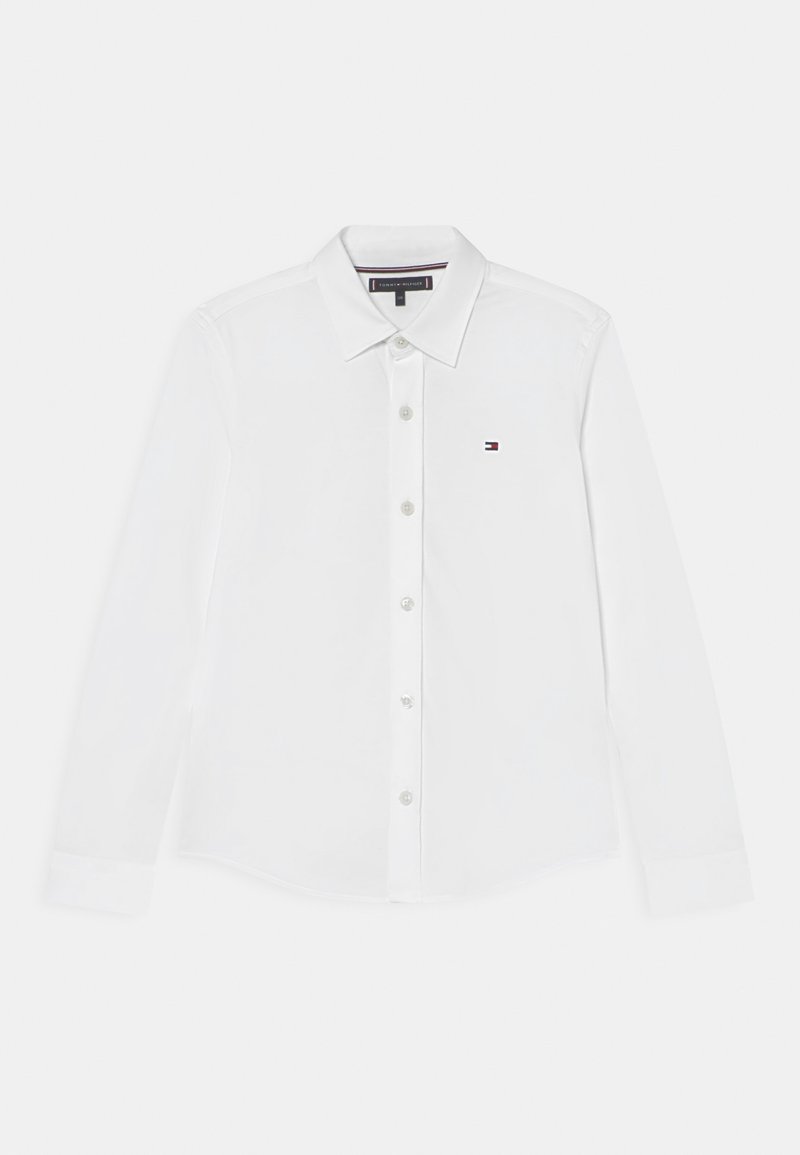 Chemise blanche à manches longues boutonnée avec col, petit logo Tommy Hilfiger sur la poitrine gauche et étiquette de marque à l'intérieur du col.