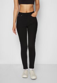 Svarta skinny jeans med hög midja, tillverkade av denim, med framfickor och en subtil röd accent. Matchas med ljusa sneakers.