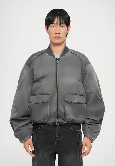 Veste bomber grise avec fermeture éclair sur le devant, deux poches avant et une texture lisse. Elle possède un col côtelé et des manches volumineuses.