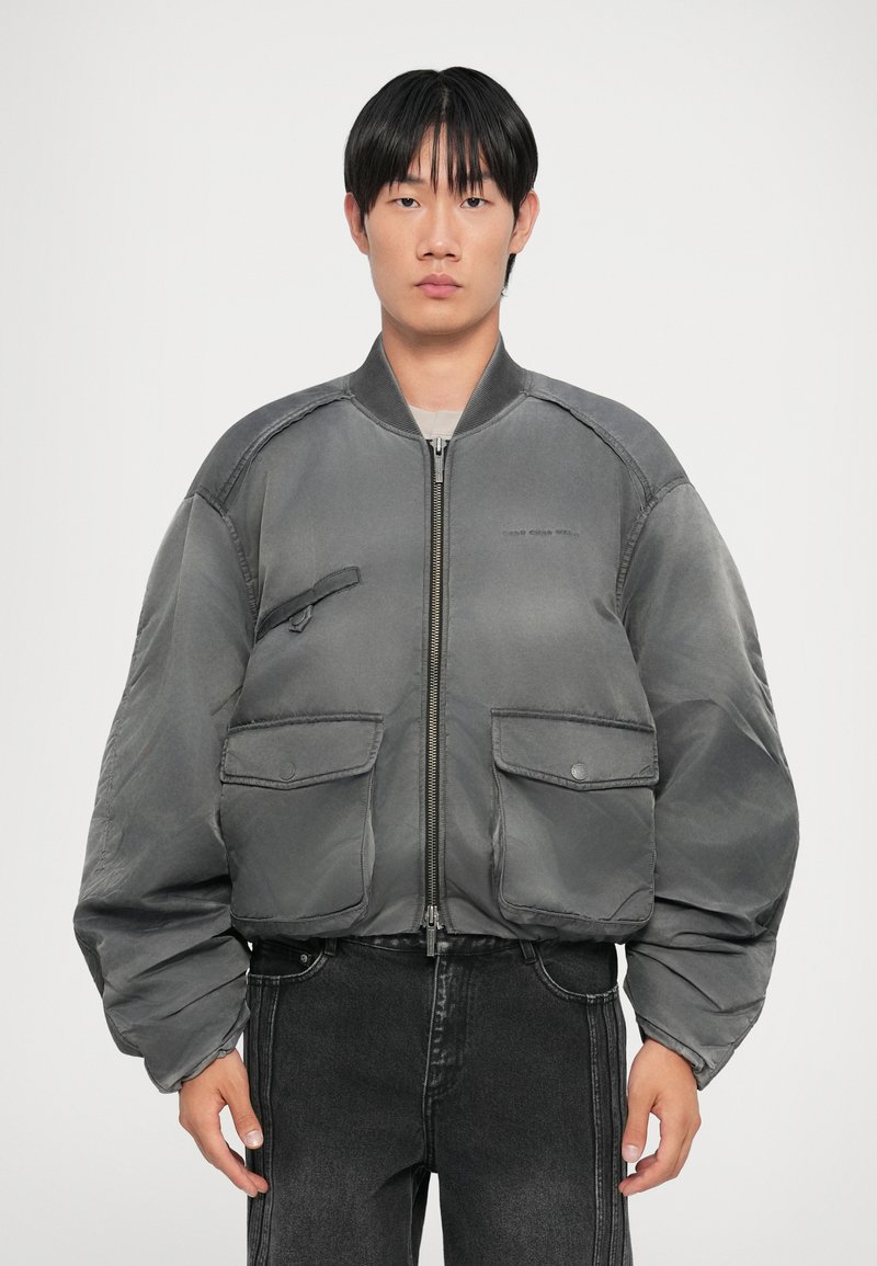 Gray bomber jacket with a zip front, two front pockets, and a smooth texture. Features a ribbed collar and voluminous sleeves.