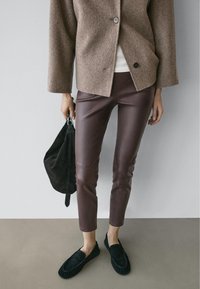 Brown wool-blend jacket with a single button, dark brown leather pants, black suede bag, and black moccasin-style shoes.