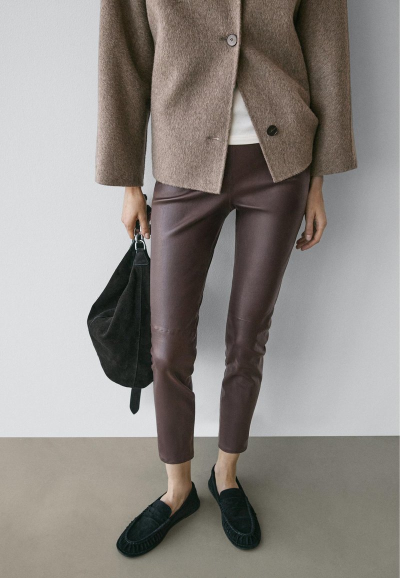 Brown wool-blend jacket with a single button, dark brown leather pants, black suede bag, and black moccasin-style shoes.