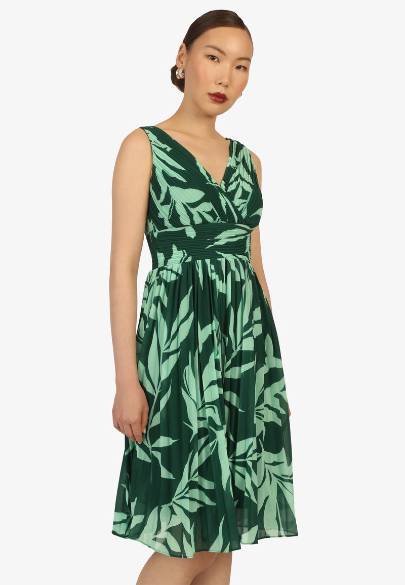 Grünes Kleid mit floralem Muster, das einen enganliegenden Oberteil und einen schwingenden Rock hat. Aus leichtem Stoff gefertigt, mit tiefem V-Ausschnitt und strukturiertem Taillenbund.