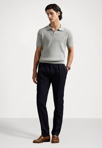 Γκρι ριπ κοφτό πόλο μπλουζάκι με κοντά μανίκια σε συνδυασμό με ναυτικό παντελόνι με λεπτές ρίγες και καφέ δερμάτινα παπούτσια. Το μοντέλο στέκεται μπροστά σε μια απλή ανοιχτόχρωμη επιφάνεια.