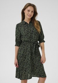 Robe verte à motif avec un devant à boutons, des manches courtes bouffantes et une ceinture à nouer, fabriquée en tissu léger avec un design fluide.