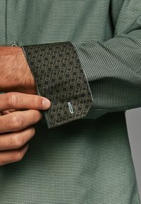 Green patterned shirt featuring a textured weave. Cuffs display a dark fabric with a gold swirl pattern and contrasting stitching detail.