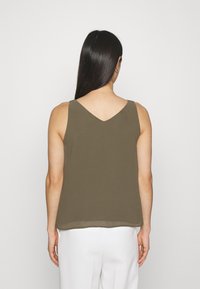 Top sin mangas en verde oliva con espalda en forma de V, que presenta una textura suave y un sutil brillo, complementado con finas tirantes.
