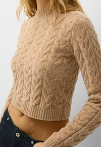 Béžový pletený zkrácený svetr s copánkovým vzorem, žebrovaným výstřihem a lemy, s texturovanou tkaninou a dlouhými rukávy.