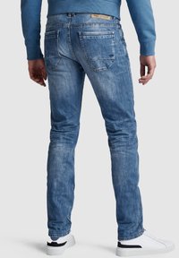 Svijetloplave traperice s izblijedjelim završetkom, pet džepova i etiketom na pojasu. Slim fit dizajn, uparen s bijelim tenisicama.