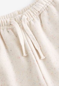 Helle beige Jogginghose mit einem gesprenkelten Muster in verschiedenen Pastellfarben. Verfügt über einen elastischen Bund und Kordeln zur Anpassung.