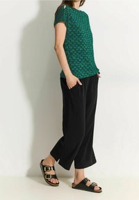 Grøn kortærmet top med bladmønster, parret med sorte brede bukser. Sorte sandaler med dobbelt guldspænde og korksåler.