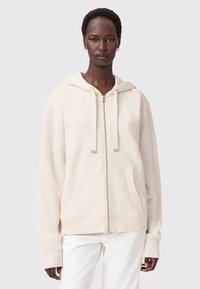 Felpa crema con zip, cappuccio regolabile e maniche a costine. Presenta un corpo liscio e due tasche frontali. Tessuto morbido.