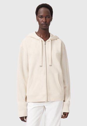 Krämfärgad zip-up hoodie med dragsko i huvan, ribbad ärmar och en slät kropp. Har två framfickor. Mjuk tygkvalitet.