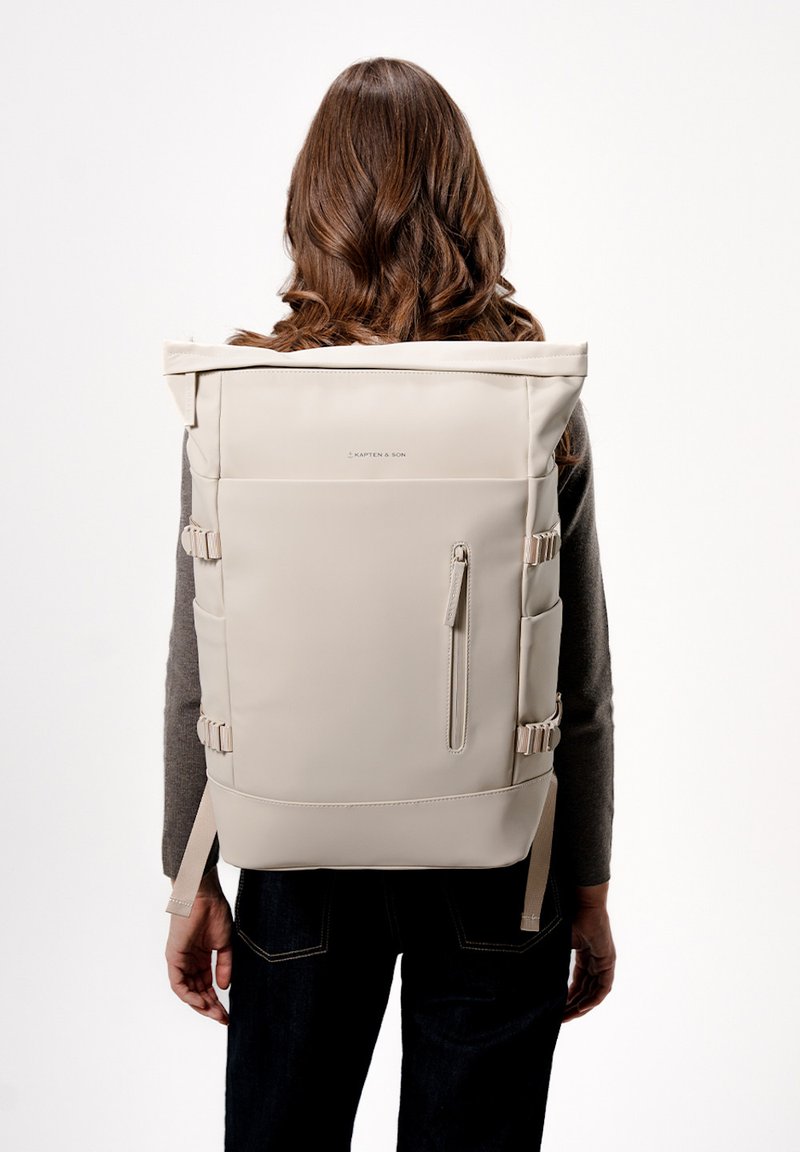 Beige rolovací batoh vyrobený z odolného materiálu. Disponuje nastavovacími popruhy, kapsou na zip a bočními sponami. Hladký texture, minimalistický design.