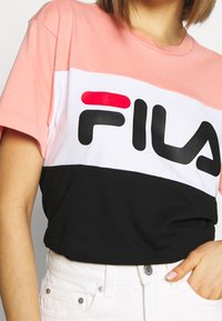T-shirt med kort ärm som har en färgblockdesign: rosa, vit och svart med en stor svart "FILA"-logotyp. Mjuk tyg med avslappnad passform.
