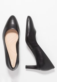 Chaussures pour femmes en cuir noir à talon moyen, une chaussure montrée de haut en bas avec une semelle intérieure rembourrée beige, l'autre vue latérale montrant la hauteur du talon.