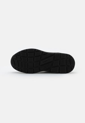 Semelle de chaussure en caoutchouc noir avec un motif texturé ; dotée de profonds sillons et crêtes pour une adhérence optimale. Marquée "superfit" sur le côté.