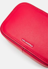 Czerwony skórzany prostokątny pokrowiec z teksturowaną powierzchnią, kontrastującymi czarnymi szwami oraz srebrną płytką z logo "KARL LAGERFELD".