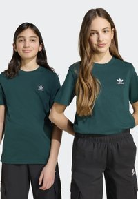 Zöld pamut pólók rövid ujjal és kerek nyakkivágással; a mellrészen egy kis fehér Adidas logó található. Fekete nadrággal viselik.