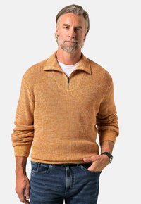 Pullover-Sweatshirt mit einem halben Reißverschlussdesign, strukturiertem orangefarbenem Strickmuster, gerippten Bündchen und Saum, kombiniert mit dunkelblauen Jeans.