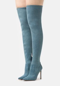 Lårhöga denimstövlar i ljusblått med en åtsittande design, spetsig tå och stilettklack; har en sidoglash för enkel påtagning.