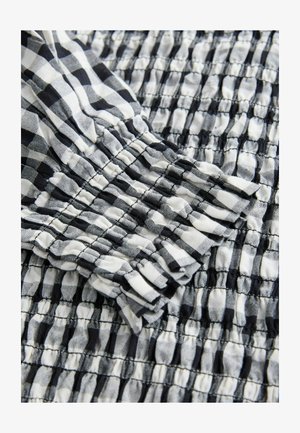 Tissu à carreaux noir et blanc avec une texture plissée, présentant un poignet à volants. Le tissu est léger et tissé.