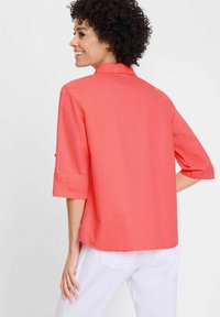 Korallenfarbens Hemd mit Kragen, drei Viertelärmeln und lockerer Passform. Hergestellt aus leichtem Stoff, mit geradem Saum und seitlichen Schlitzen.