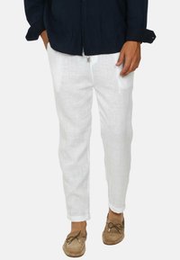 Pantaloni bianchi in lino con una vestibilità rilassata, dotati di tasche laterali, orli arrotolati e tessuto testurizzato; abbinati a scarpe mocassino marrone chiaro.
