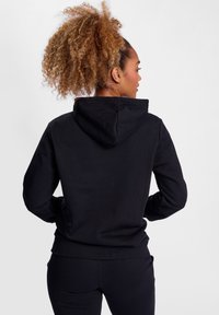 Svart hoodie med dragsko i huvan, mjukt tyg och ribbade muddar och fåll. Minimalistisk design; inga synliga logotyper eller mönster.