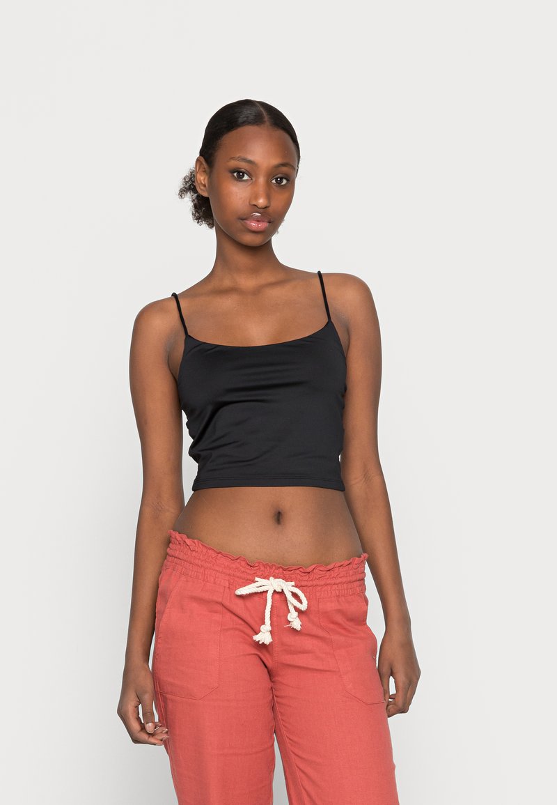 Top cropped preto com alças finas ajustáveis. Combinado com calças de um vermelho claro que apresentam um cós com frufru e detalhe de cordão.