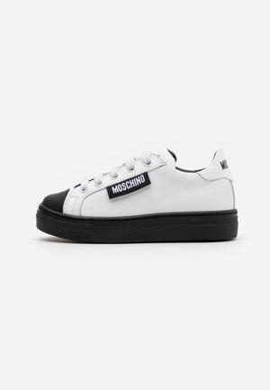 Białe skórzane sneakersy z czarną gumową osłoną na palce i podeszwą. Posiadają czarną metkę z logo przyszytą po zewnętrznej stronie. Okrągłe sznurówki.