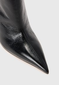 Black leather ankle boot with a pointed toe, smooth texture, and a synthetic lined interior. Features a seamless design with minimal stitching.