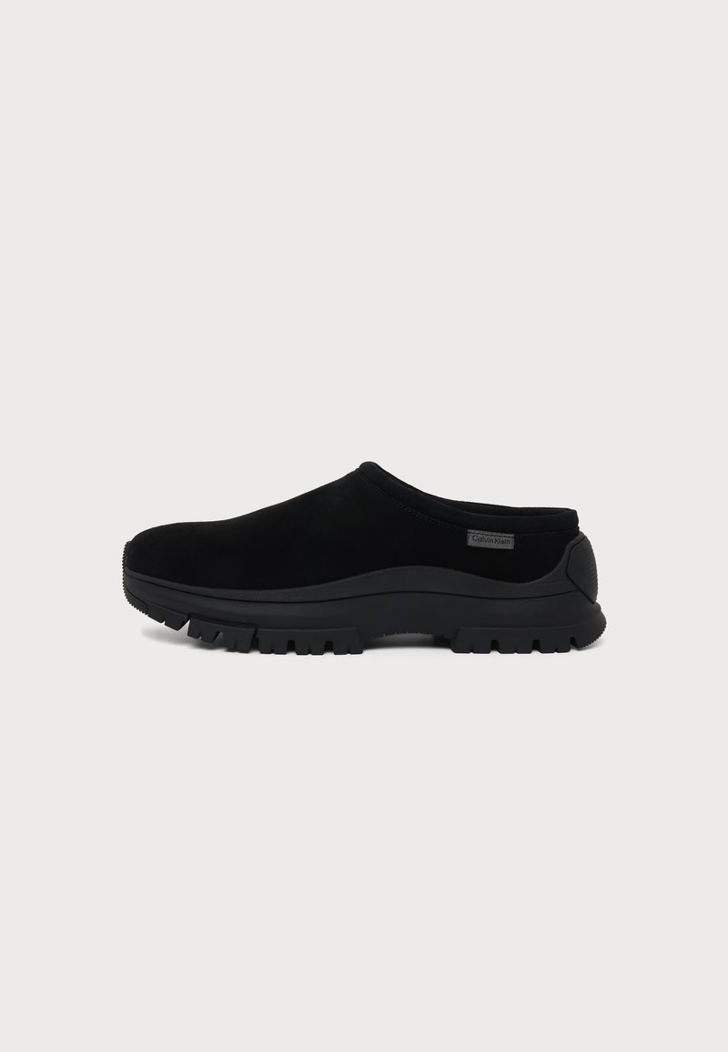 Μαύρο παπούτσι slip-on με χοντρή σόλα και χαμηλή φτέρνα, με μικρό λογότυπο στην πλευρά κοντά στη φτέρνα.