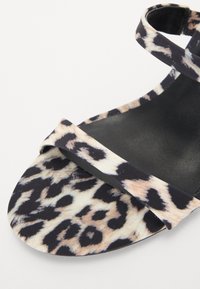 Åpen tå sandal med leopardmønster, med svart bunn, slanke stropper og en jevn tekstur.