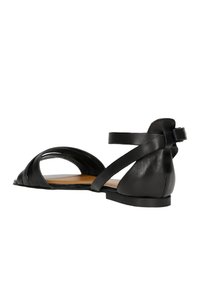 Czarne skórzane sandały z krzyżującymi się paskami i tylnym paskiem na kostkę. Płaska podeszwa o gładkiej teksturze i częściowo otwartym designie.