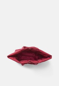 Borsa tote rossa in nylon, vista aperta che rivela un ampio interno. Presenta una superficie liscia e un design minimalista con chiusura superiore a stringa.