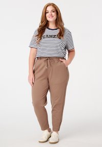Pantalons de jogging marron avec poches latérales et cordon de serrage. Associé à une chemise à rayures à manches courtes avec un motif scintillant. Baskets blanches.