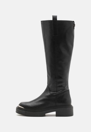 Botas de cuero negras hasta la rodilla con una textura suave, punta redondeada, suela de plataforma gruesa y una pestaña de agarre en la parte superior para facilitar su uso.