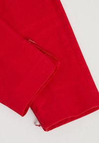 Rode stoffen broek met een zijzak met rits. Soepele textuur met een getailleerde pasvorm, detail zichtbaar bij de zoom.