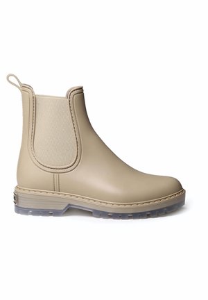 Bottine Chelsea en caoutchouc beige avec des panneaux latéraux élastiques, une languette à l'arrière et une semelle translucide. Texture lisse avec des détails de couture renforcée.